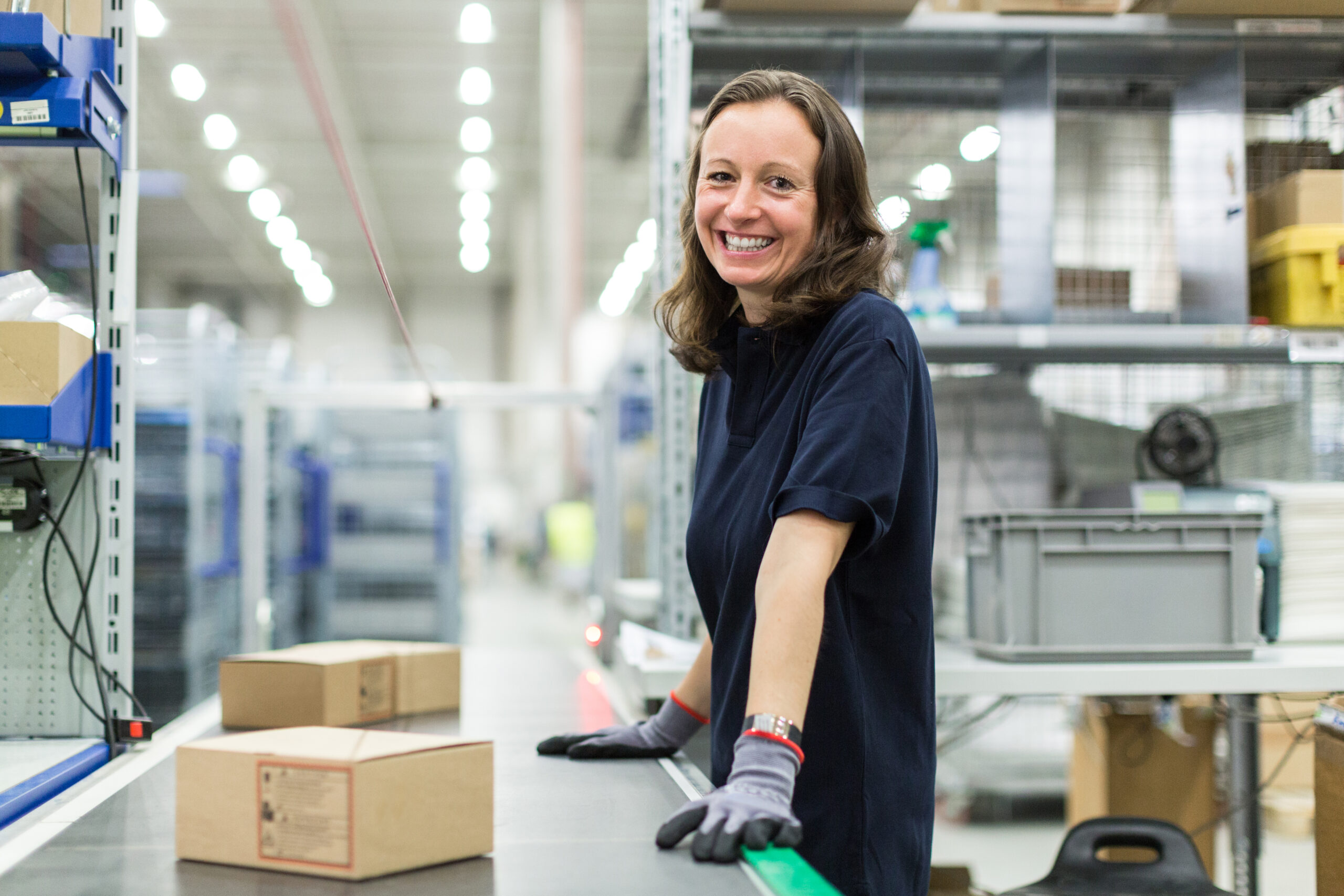 zensmart is showing A woman wearing gloves and a navy shirt smiles while standing at a packing station in a warehouse, with cardboard boxes and storage shelves visible in the background. with print workflow automation